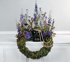 a wreath with purple flowers and greenery hanging on a wall in front of a white door