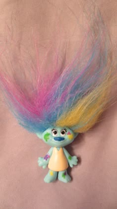 a troll doll with multicolored hair on it's head sitting on a pink surface