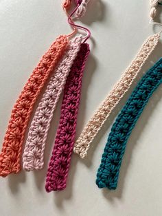 three crocheted hair ties are laying on a white surface, one is pink and the other is blue