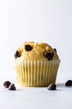 a muffin with chocolate chips on top sitting on a white surface next to it