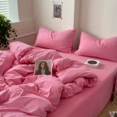 a bed covered in pink sheets and pillows next to a potted plant on the floor