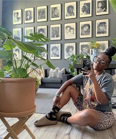 a woman sitting on the floor in front of a potted plant talking on her cell phone