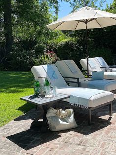 lounge chairs and an umbrella are sitting on the brick patio in front of some trees