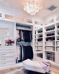 a walk in closet filled with lots of white shelves and drawers next to a chandelier