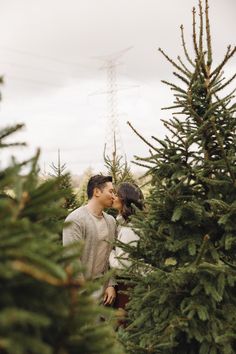 a man and woman standing next to each other in front of a christmas tree farm