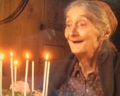 an old woman sitting in front of a cake with lit candles