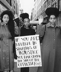 black and white photograph of three women holding protest signs in the middle of an urban street