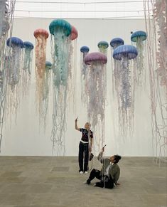 two people sitting on the ground in front of jellyfish suspended from ceiling above them