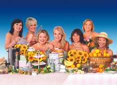 a group of women standing next to each other in front of a table covered with sunflowers