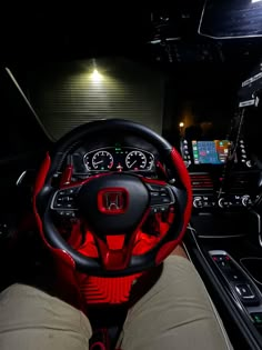 the interior of a car is lit up with red and black lights, while someone's feet are on the steering wheel