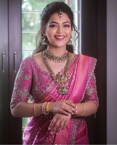 a woman in a pink sari smiling for the camera with her hands folded out