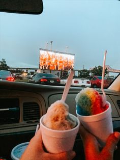 two ice cream cones with rainbow colored toppings in front of a large screen at an outdoor concert