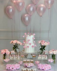 a white cake surrounded by pink flowers and balloons