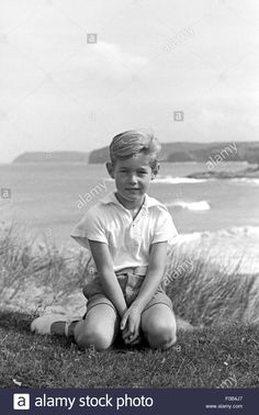 a young boy sitting on the grass by the ocean with his feet crossed - stock image