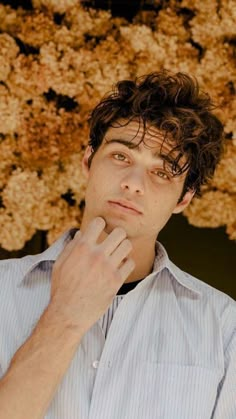 a man with curly hair is looking at the camera and has his hand on his chin