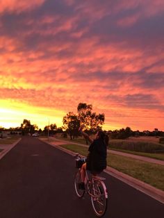 a person riding a bike down a street at sunset with the sun setting in the background