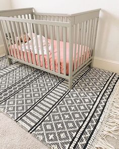 a baby's crib in a white room with pink pillows and blankets on the floor