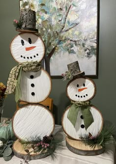 three snowmen made out of wood sitting on top of a table next to a painting