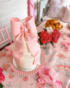 a table topped with a cake covered in pink ribbon next to flowers and other food