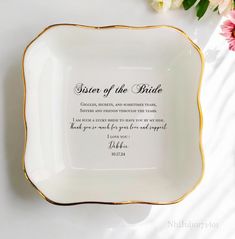 a white and gold plate with the words sister of the bride on it next to flowers