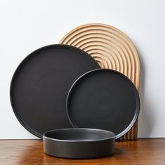 three black plates sitting on top of a wooden table next to a plate holder and wall