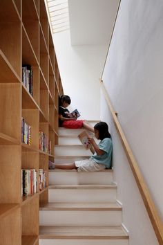 children are sitting on the stairs in front of bookshelves and looking at them