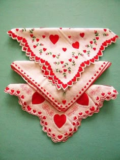 three napkins with hearts on them sitting on a green tablecloth covered wall in the shape of an ornament