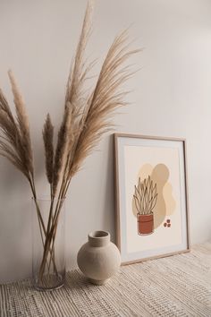 there is a vase with some dry grass in it next to a painting on the wall