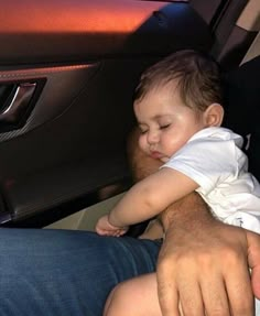 a man holding a small child in his lap while sitting in the back seat of a car