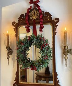 a mirror hanging on the wall with a wreath in front of it and two candles