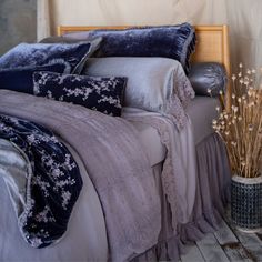 a bed with blue and grey comforters in a bedroom next to a vase filled with dried flowers