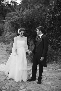 black and white photo of bride and groom holding hands on cobblestone path with trees in background