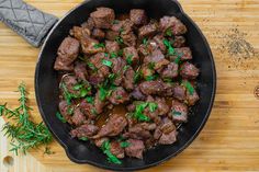 meat and herbs cooking in a skillet on a cutting board