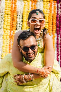 a man carrying a woman on his back in front of colorful garlands and flowers