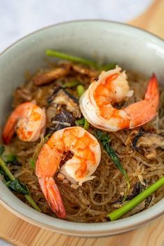 a bowl filled with noodles and shrimp on top of a wooden table next to chopsticks