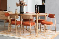 a dining room table with orange chairs and a vase on top of the table in front of it