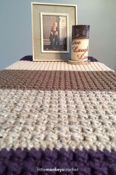 a crocheted blanket with a photo frame next to it on top of a bed