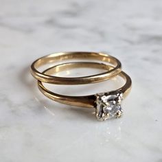 two gold wedding rings with a single diamond in the center on a white marble surface