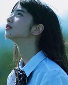 a woman with long black hair wearing a white shirt and tie looking up at the sky