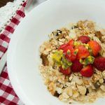 a white bowl filled with oatmeal and strawberries on top of a checkered table cloth