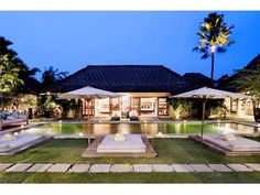 an outdoor swimming pool with lounge chairs and umbrellas around it at night, surrounded by palm trees