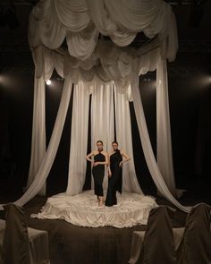 two women standing in front of white drapes