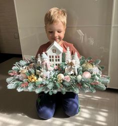 a young boy sitting on the floor holding a house shaped arrangement in front of him