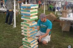 a man kneeling down next to a tall tower made out of wooden blocks on top of grass