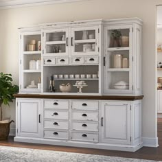 an old white china cabinet with glass doors and drawers in the middle of it, next to a potted plant