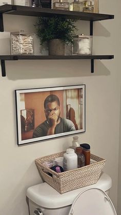 a white toilet sitting next to a bathroom wall with shelves above it and a framed photo on the wall