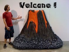 a man standing in front of a fake volcano with the words volcano on it's side