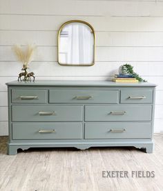 the dresser is painted gray with gold handles and pulls on it's drawers, along with a mirror