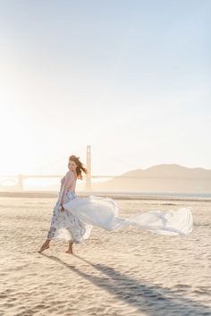 a woman is walking on the beach with her dress blowing in the wind