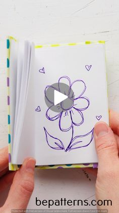 someone is holding an open book with a flower drawn on it and the video below shows how to draw a flower